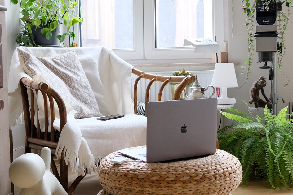 A laptop on a footstall surrounded by indoor plants.