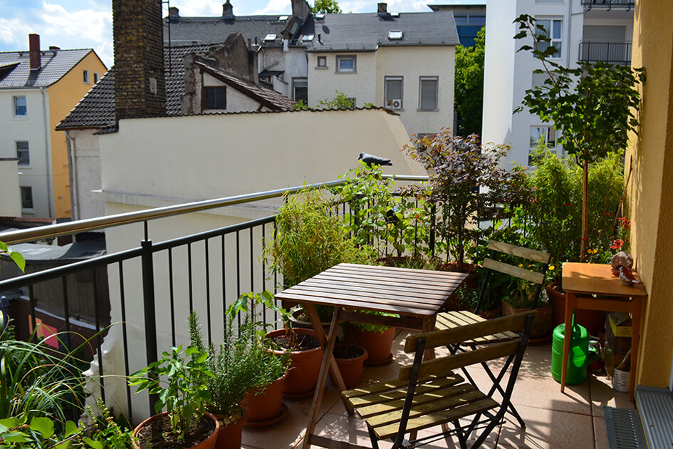 A balcony with plants and a table and chairs.