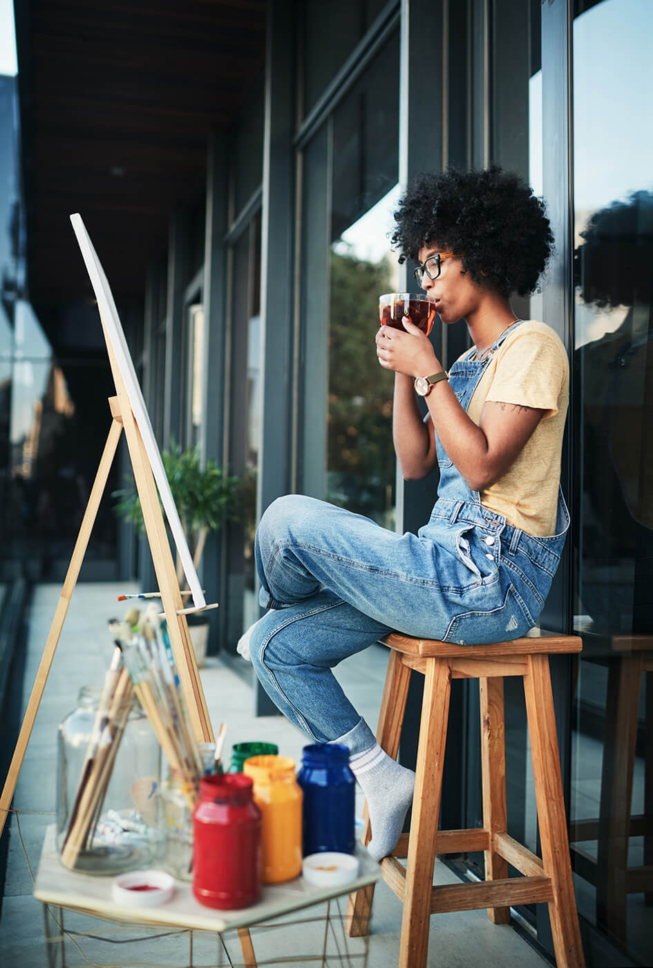 A lady painting on an easel on her balcony drinking tea.