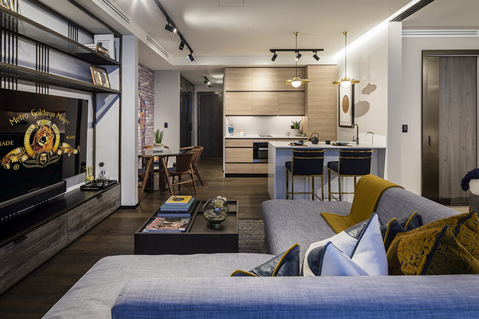 An industrial style open-plan apartment at The Stage in Shoreditch featuring a grey sofa, breakfast bar and oak kitchen units.