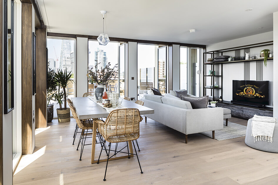 A stylish living and dining area with doors opening onto a large balcony with direct views of The Shard at Trilogy in London.