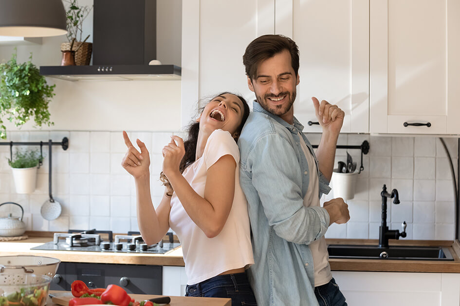 A couple laughing and dancing in their kitchen.