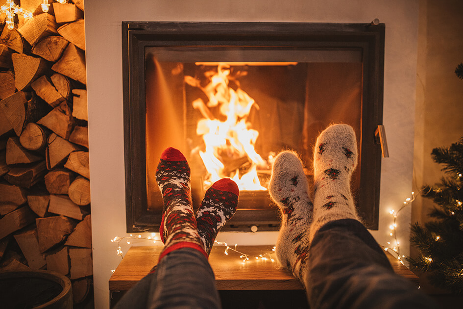 Two people wearing festive socks in front of the fireplace.