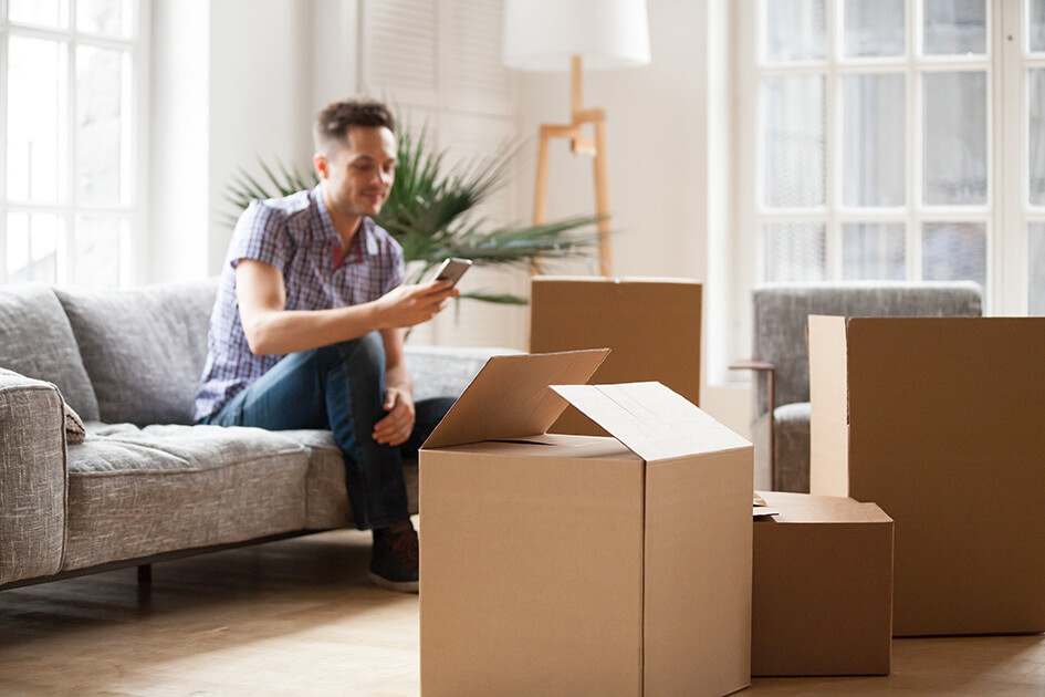 A man looking at a phone surrounded by moving boxes.