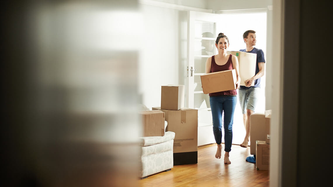 A couple carrying boxes and moving into a new house.