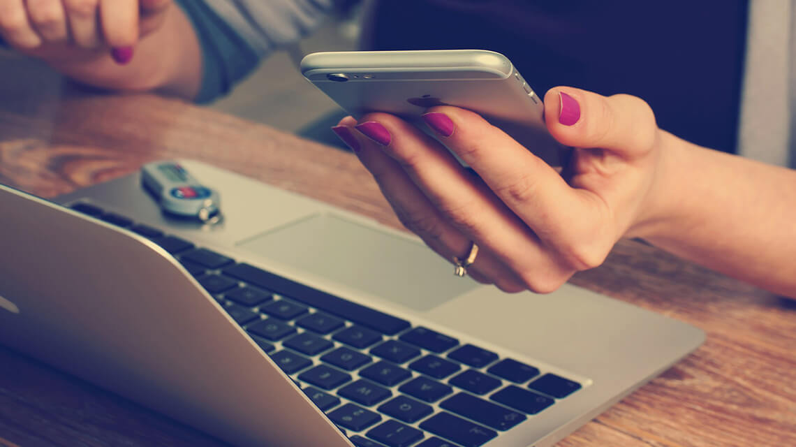 A person sitting at a laptop holding a phone.