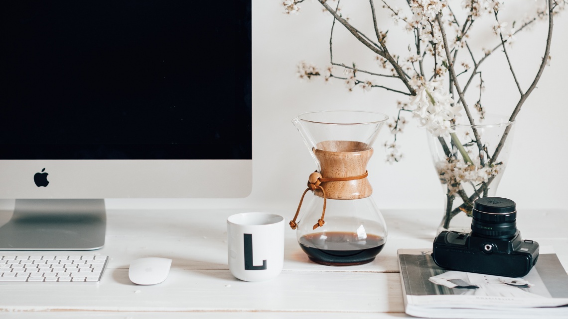 A desk with a computer, camera and coffee.