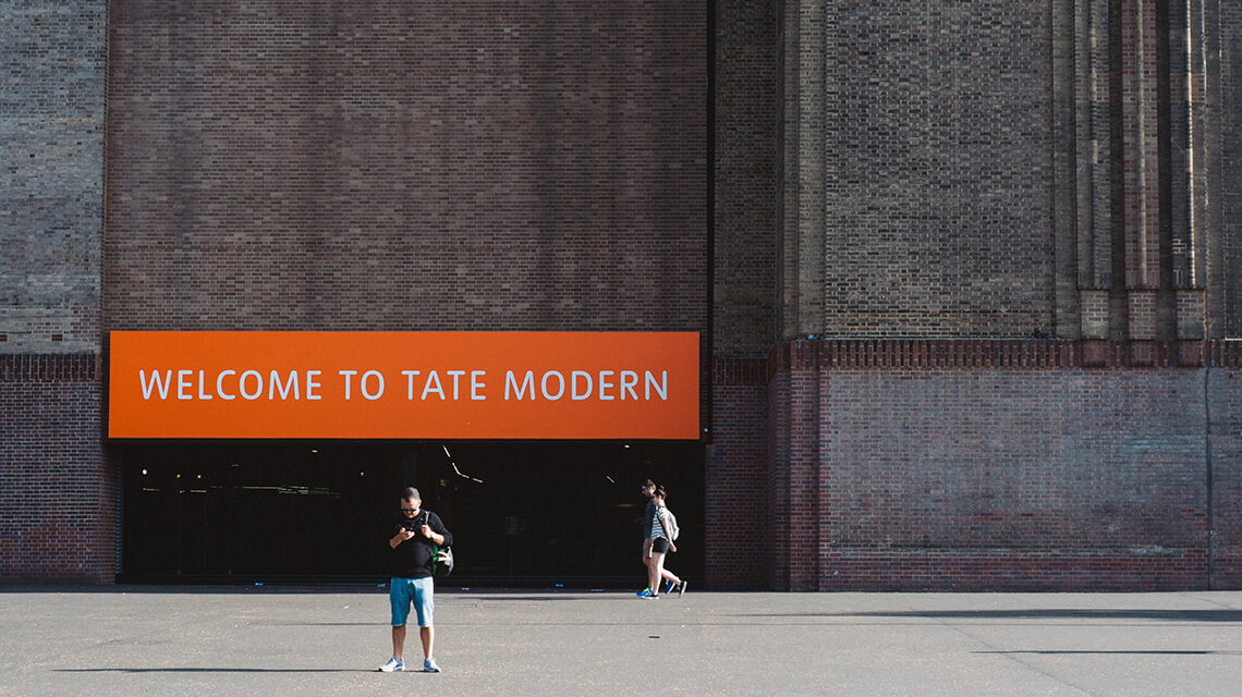 A person standing underneath a sign saying 'Welcome to Tate Modern' in London.