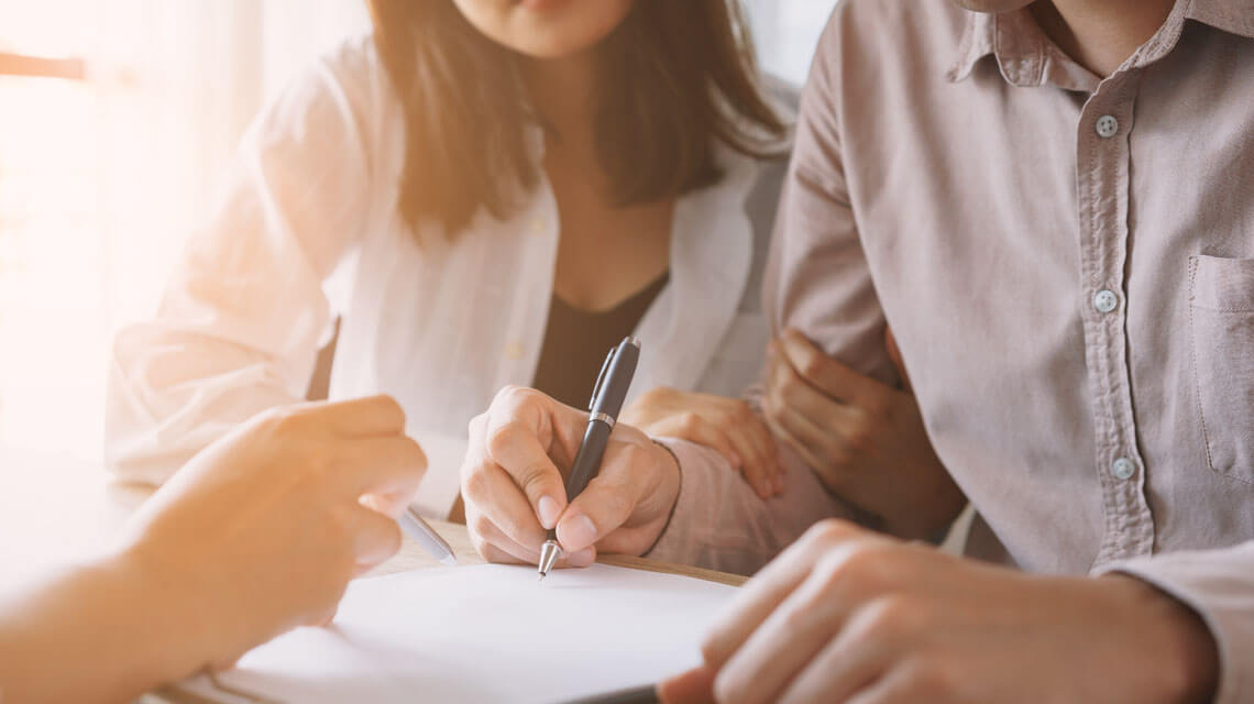 Overseas couple signing contacts for their new property purchase