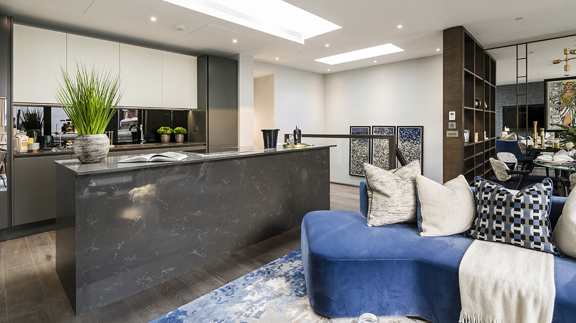 Living and kitchen area featuring a blue sofa and kitchen island at a luxury apartment at Hanway Gardens, a Galliard Homes development in London.